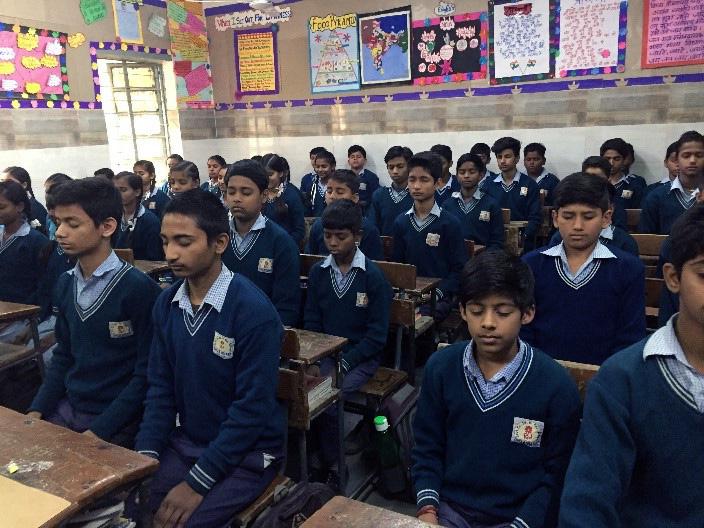 children sit at desks with eyes closed and hands in laps