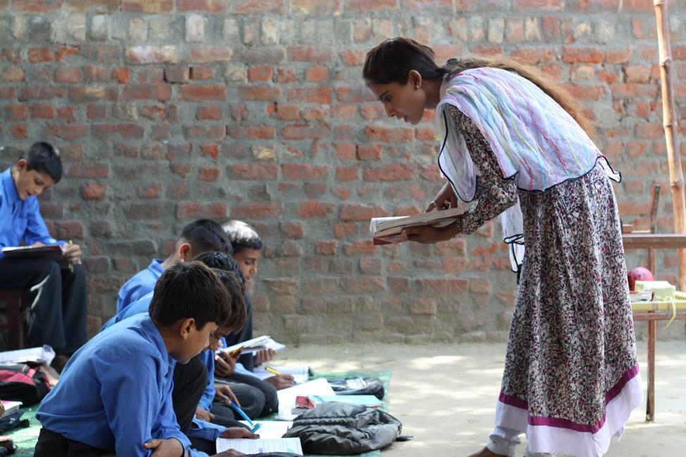A teacher at a school in Kasur, Punjab stands over a class doing work