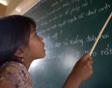 A girl points at a blackboard covered in writing. Photo by Chau Doan / World Bank